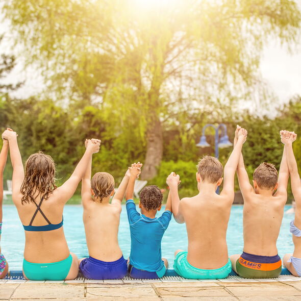 Eine Gruppe Kinder sitzt am Beckenrand eines Freibades und hat die Arme in der Luft