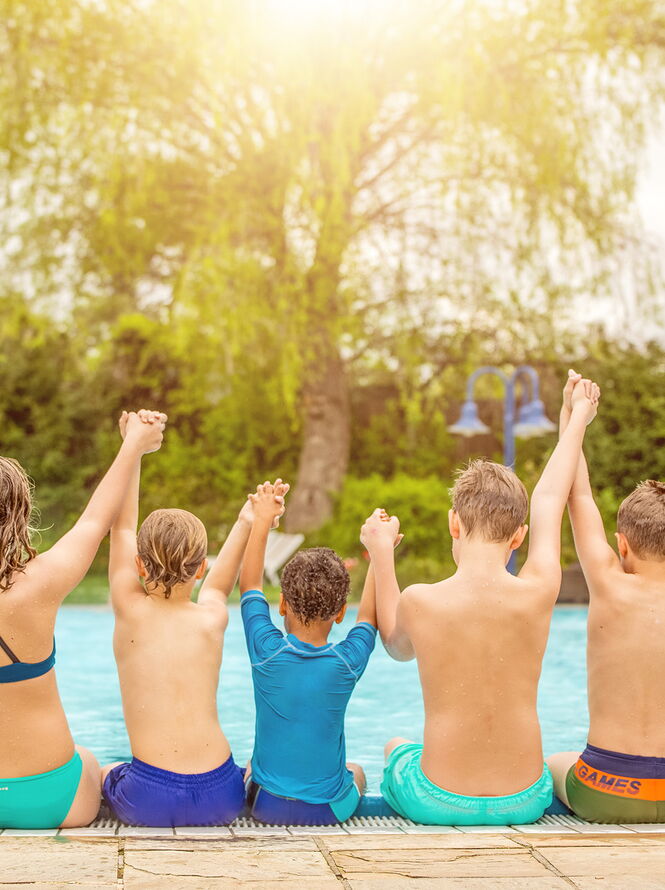 Eine Gruppe Kinder sitzt am Beckenrand eines Freibades und hat die Arme in der Luft